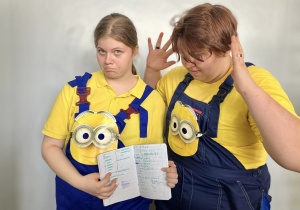 Uczennice w przebraniu Minionków pokazują zeszyt od matematyki rekwizyt przedstawienia
