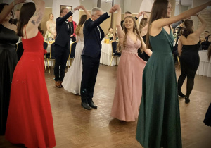 Uczniowie klas czwartych tańczą poloneza w sali balowej.